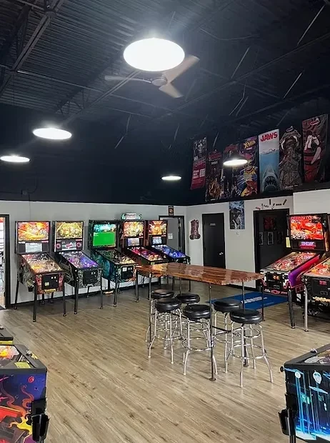 Empty arcade bar featuring colorful pinball machines and a communal high-top table.