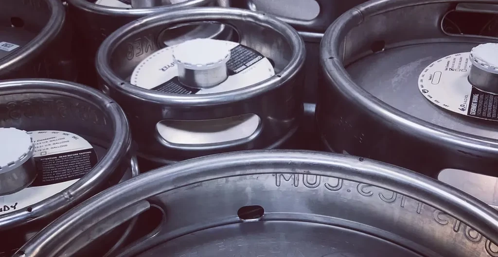 Dense cluster of metallic beer kegs with white caps and warning labels.