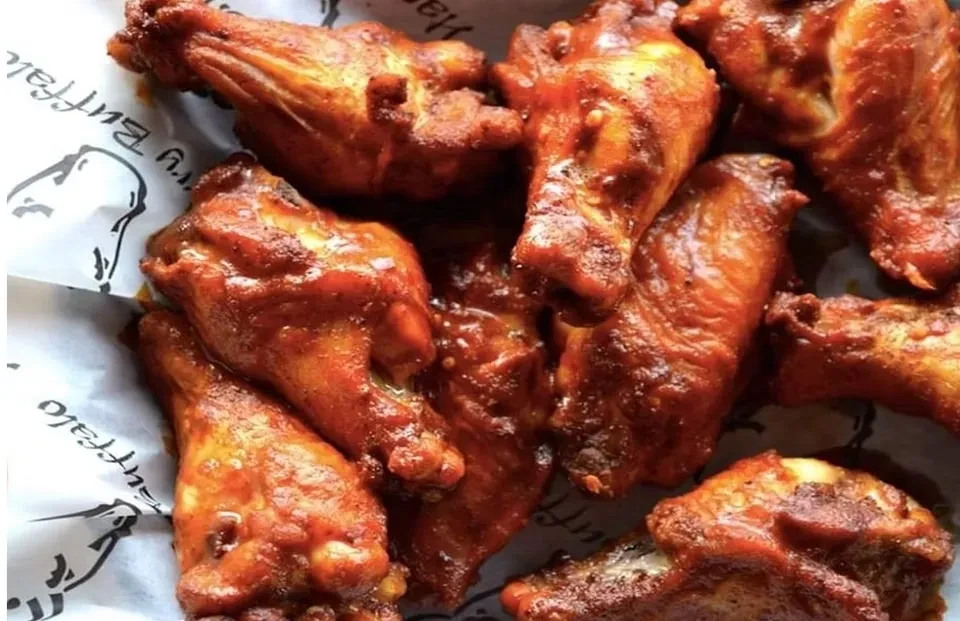 Crispy, charred chicken wings with a reddish-brown glaze in a container.