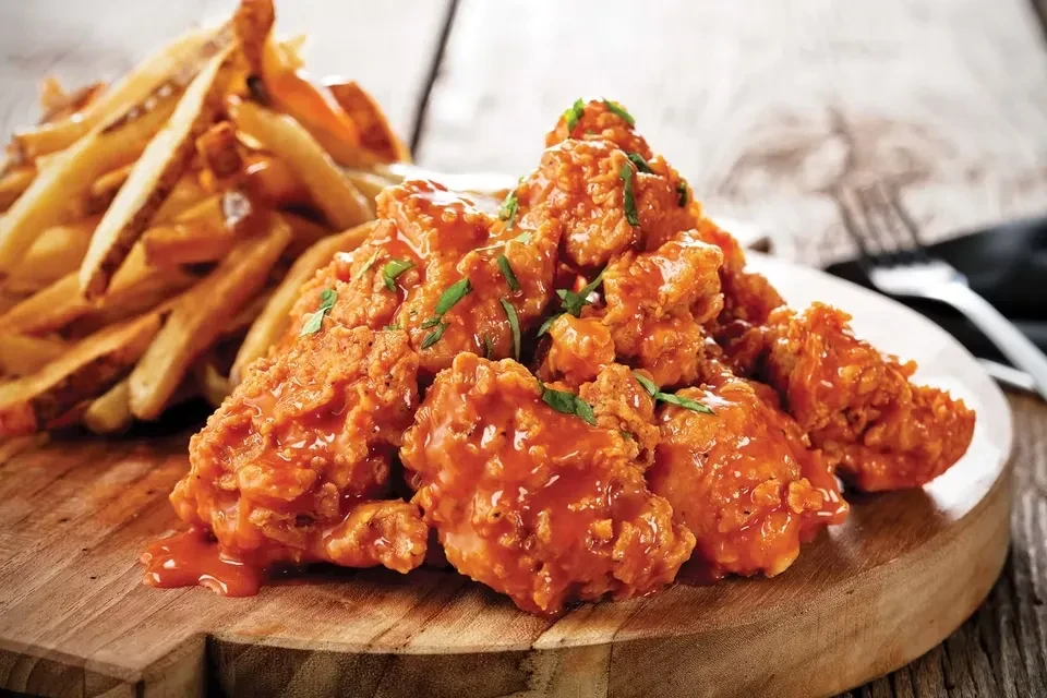 Vibrant orange-red sauced fried chicken and fries on a wooden board.
