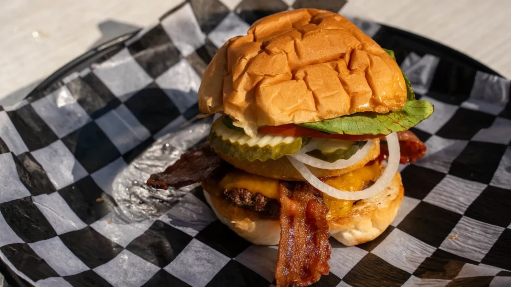 Close-up of a bacon cheeseburger with melted cheese, bacon, and vegetables.