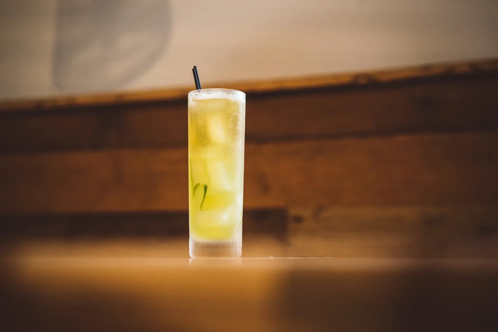 Cold yellow-green drink with ice, cucumber slices, and a black straw.