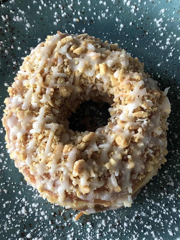 Round donut with white glaze, crunchy golden pieces, and stringy topping.