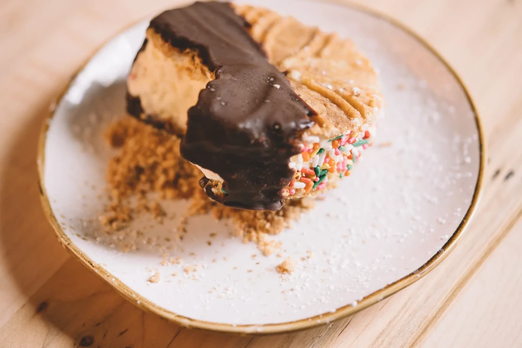 Chocolate-covered dessert bar with cookies, creamy filling, and colorful sprinkles.