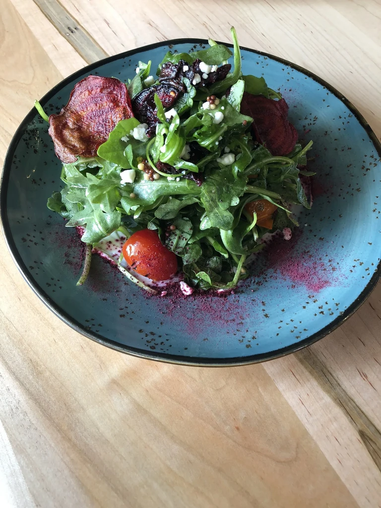 Arugula salad with beet chips, feta, berries on teal plate.