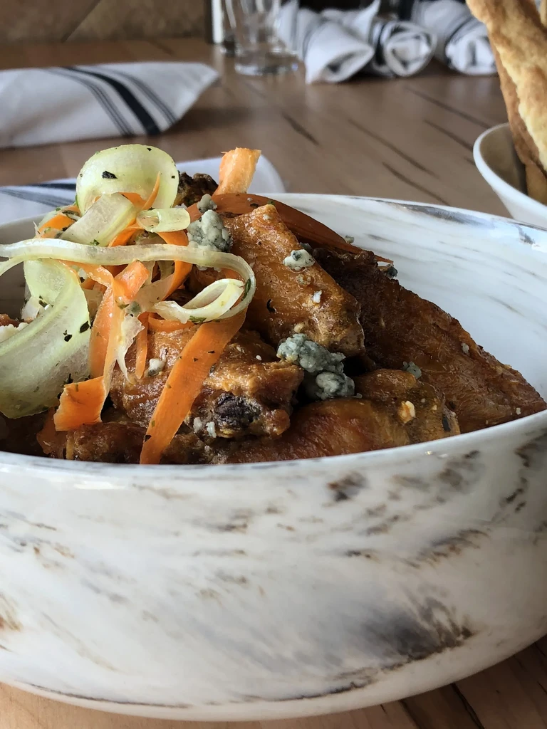 Chicken wings with blue cheese, vegetable slaw, in a marbled white bowl.