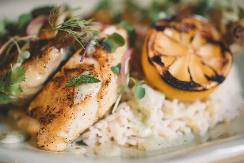 Grilled fish or chicken fillets with rice, creamy green sauce, and lemon.
