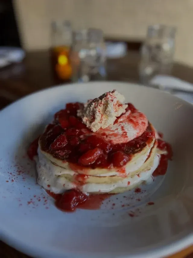 Stacked dessert with red berry compote and whipped cream in a bowl.