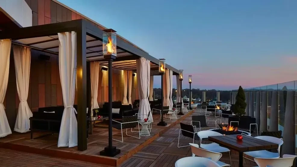 Modern rooftop patio with pergolas, fire pits, and twilight landscape.