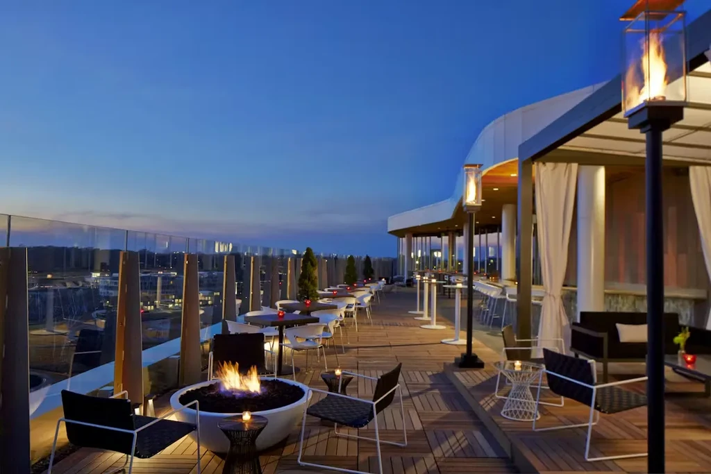 Empty rooftop patio at dusk with fire pit, lounge, city view.