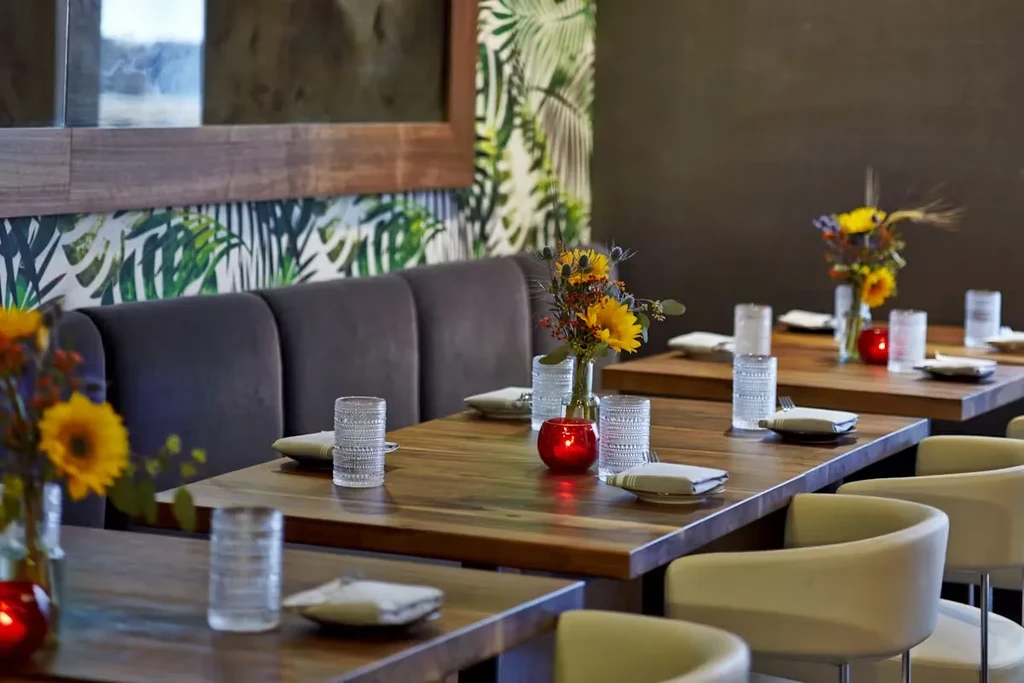 Modern restaurant interior with set tables, floral arrangements, and tropical wallpaper.
