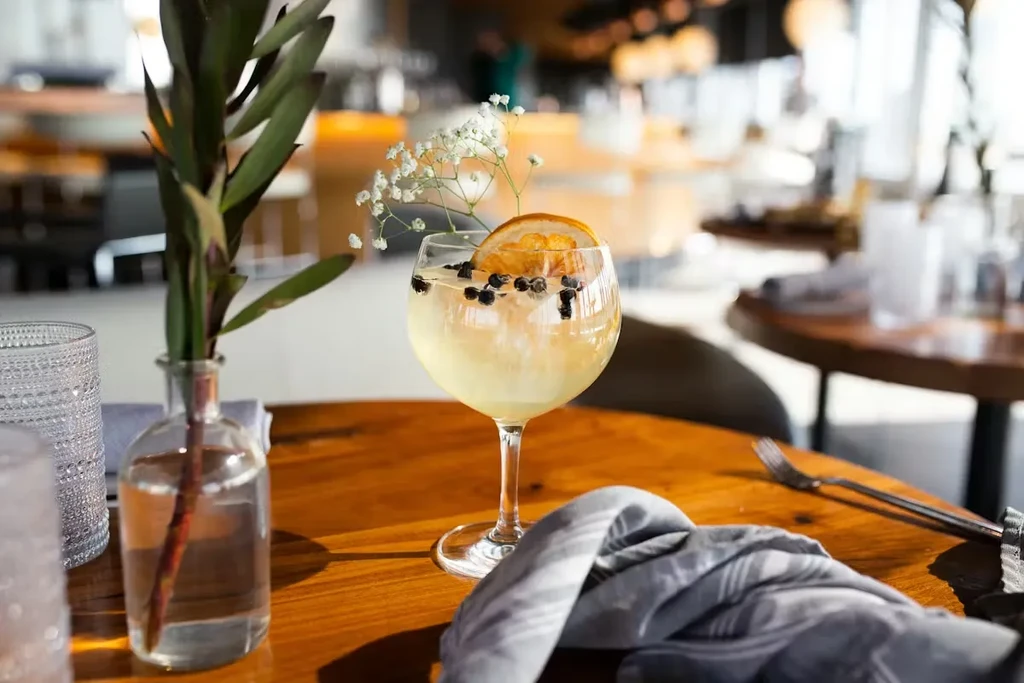 Stemmed cocktail with orange, berries, and flowers on a restaurant table.