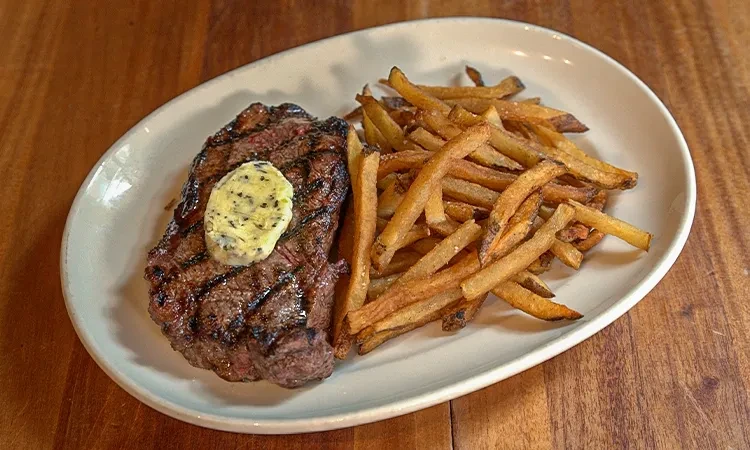Grilled steak with herbed butter and golden french fries on a plate.