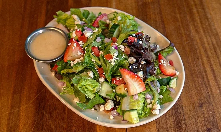 Mixed green salad with strawberries, feta, cucumber, onion, and dressing.