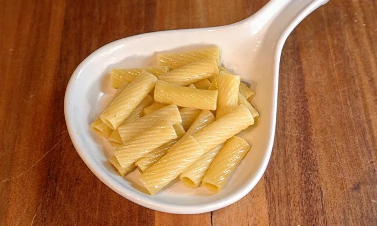 Cooked ridged rigatoni pasta in a white dish on a wooden surface.