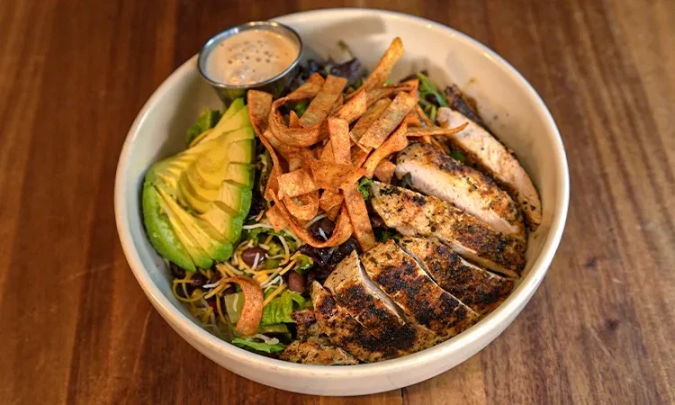 Close-up of grilled chicken, avocado, and tortilla strip salad with dressing.