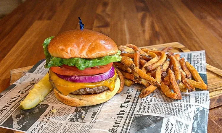 A cheeseburger, french fries, and a pickle spear on a wooden board.