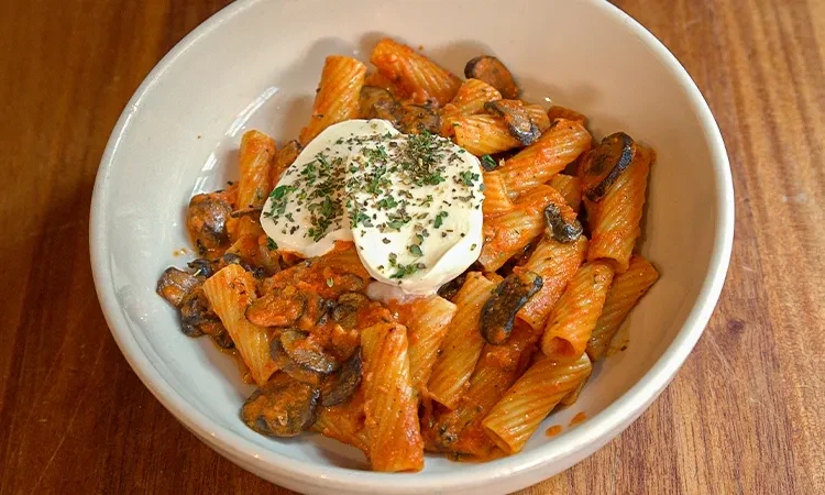 Overhead rigatoni pasta with creamy orange sauce, mushrooms, cheese, and herbs.