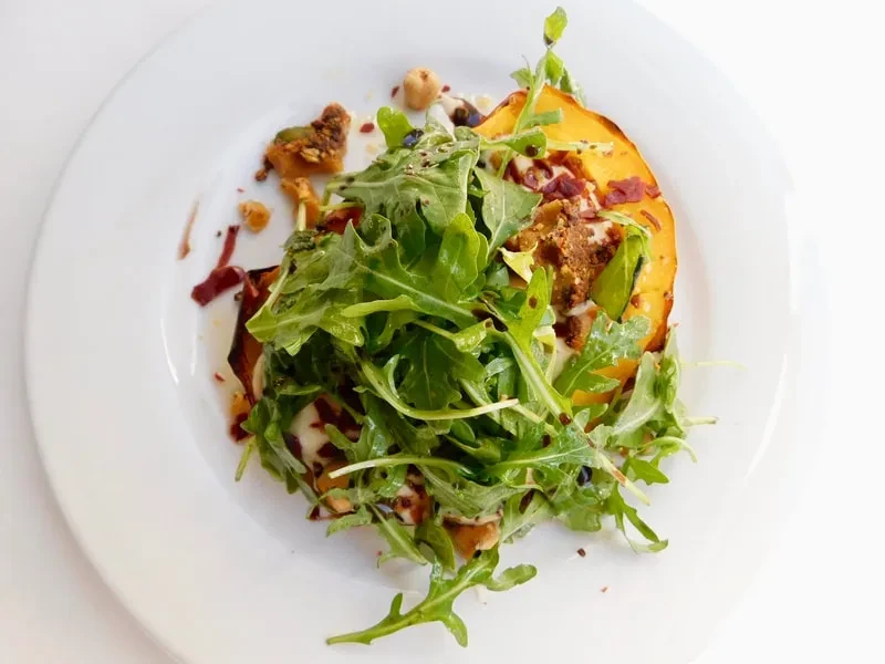 Overhead view of a plated dish with roasted squash, arugula, and diverse toppings.