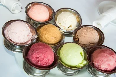 Eight colorful ice cream and sorbet servings in silver pedestal cups.