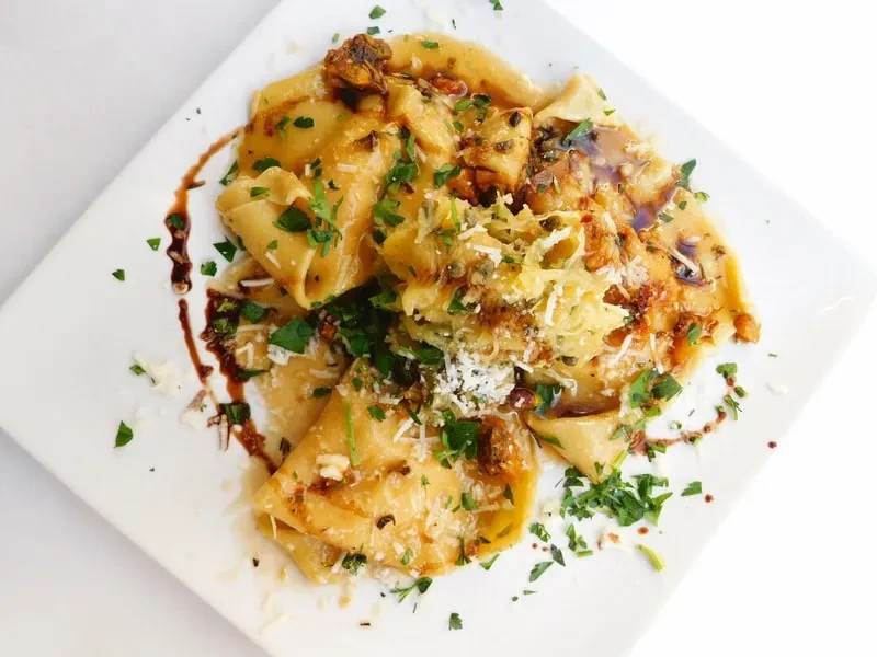 Close-up: Pasta with creamy sauce, cheese, herbs, and balsamic drizzle.