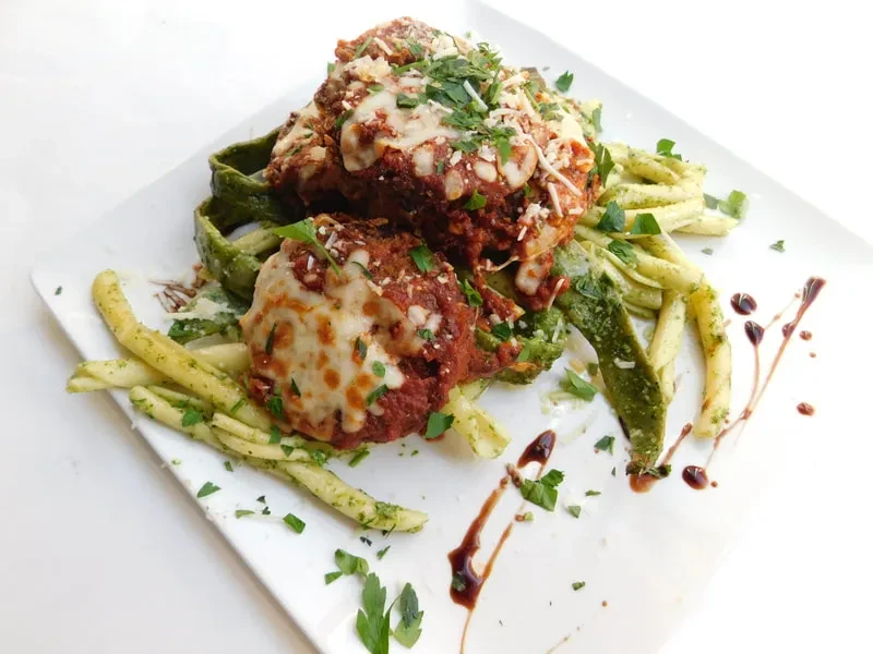 Two meatballs in tomato sauce, melted cheese, herbs, and pasta.