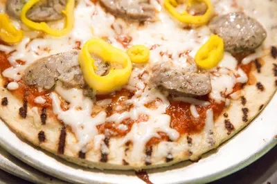 Personal pizza with grilled crust, tomato sauce, mozzarella, sausage, yellow peppers.