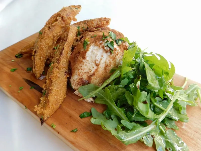 Fried items, spiced protein, and green salad on a wooden board.