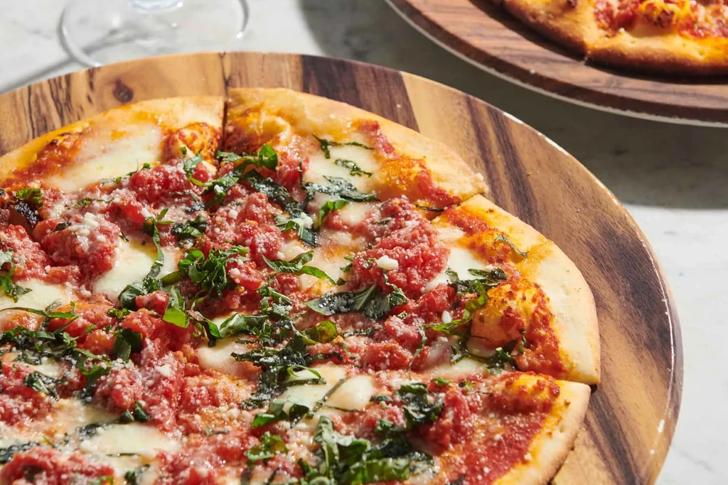 Sliced pizza with tomato, mozzarella, basil on wooden board, wine glass.