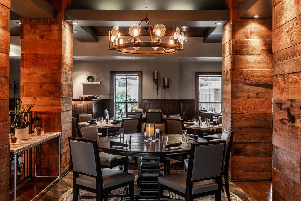 Empty restaurant dining area with rustic wood and ornate chandelier, set tables.