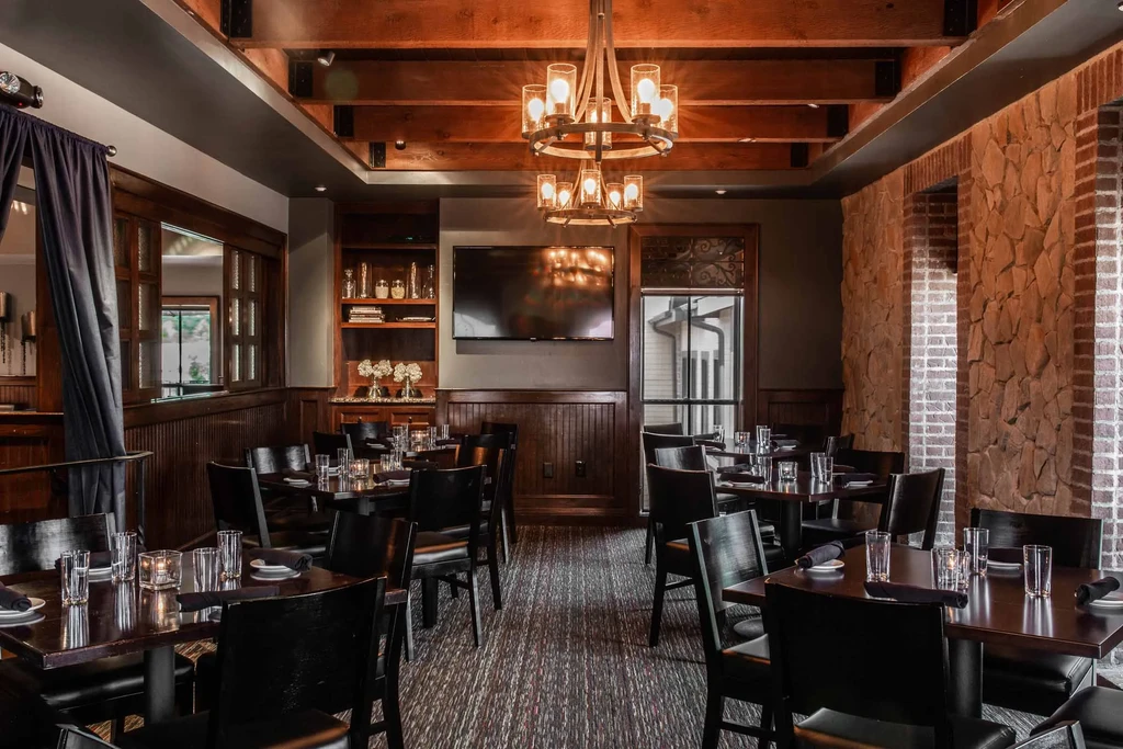 Elegant rustic-modern restaurant interior with chandelier and set tables.