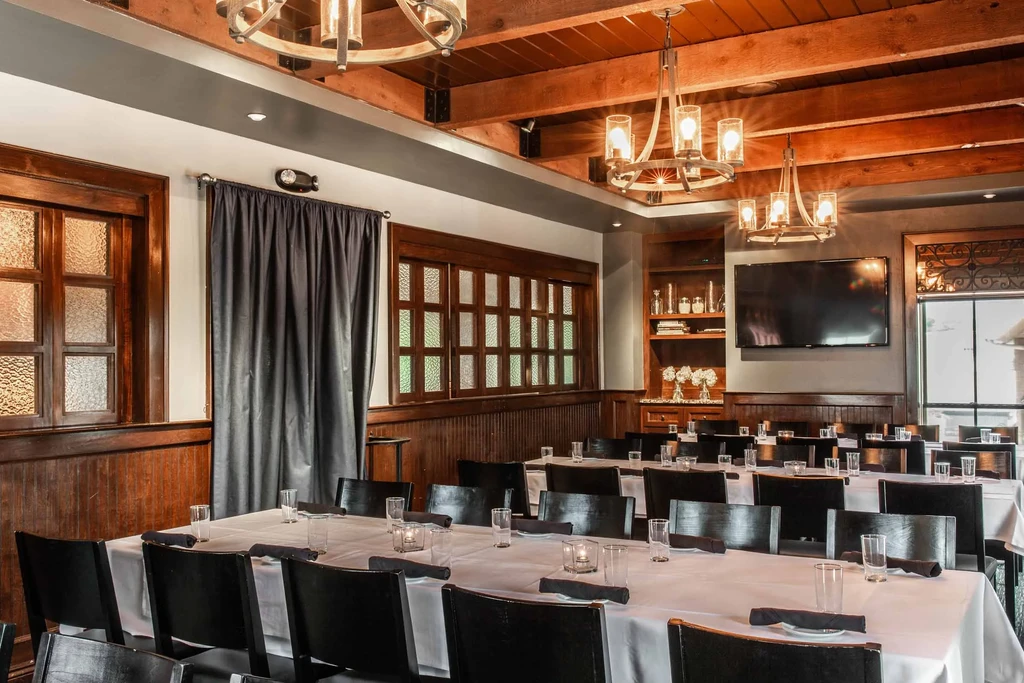 Elegant dining room with white tables, dark chairs, wood paneling, chandeliers.