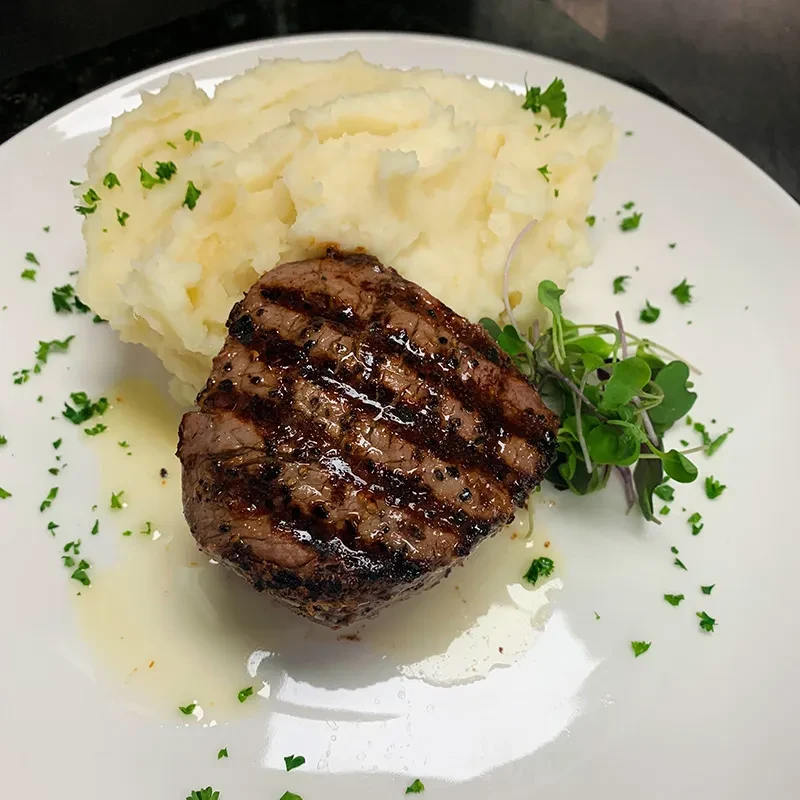 Professionally plated grilled steak, mashed potatoes, microgreens, and herbs.