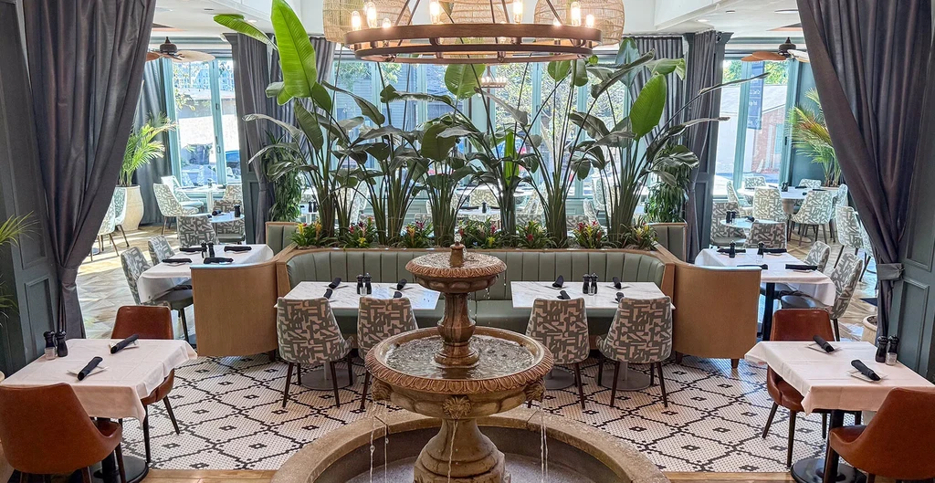 Empty, stylish restaurant interior with ornate fountain and tropical plants.