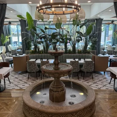 Bright, modern restaurant interior with a prominent multi-tiered stone fountain.