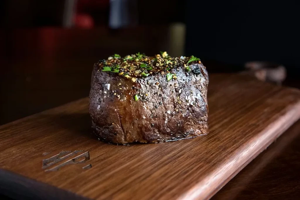 Juicy, seared steak with peppercorns and herbs on a wooden board.