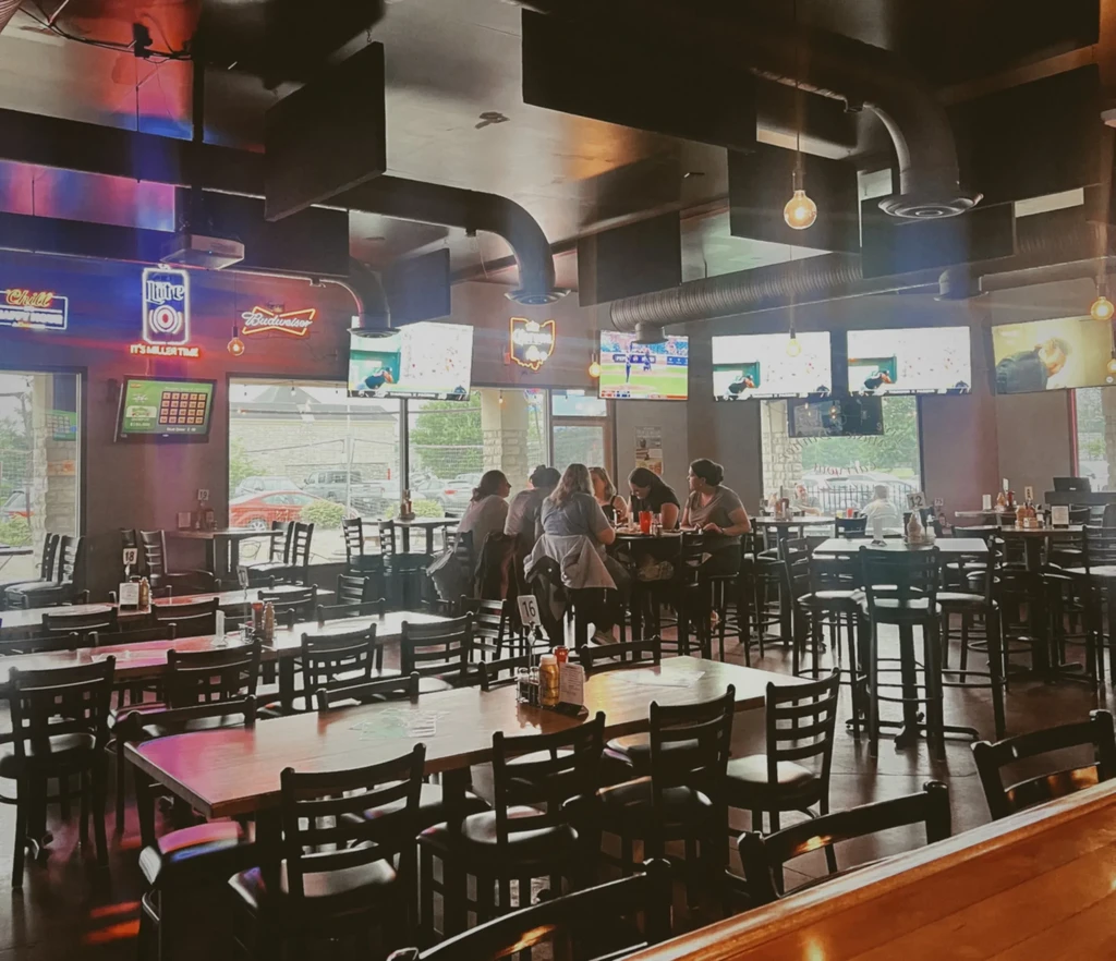 Sports bar interior with multiple TVs, neon signs, and customers.