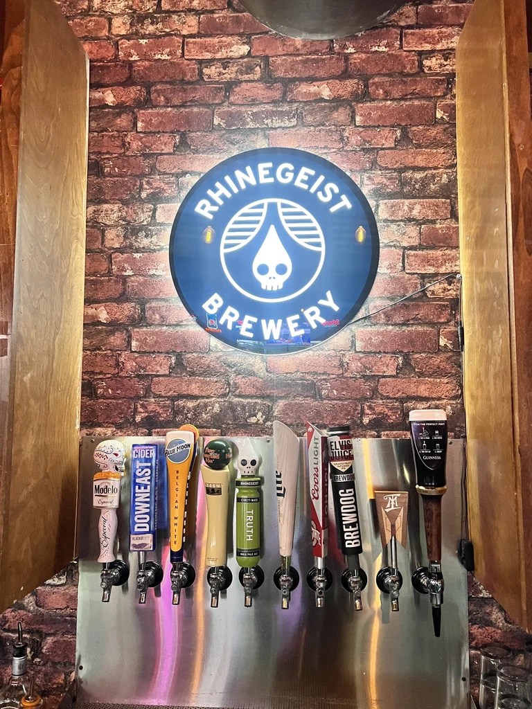 Ten beer taps below an illuminated Rhinegeist Brewery sign.