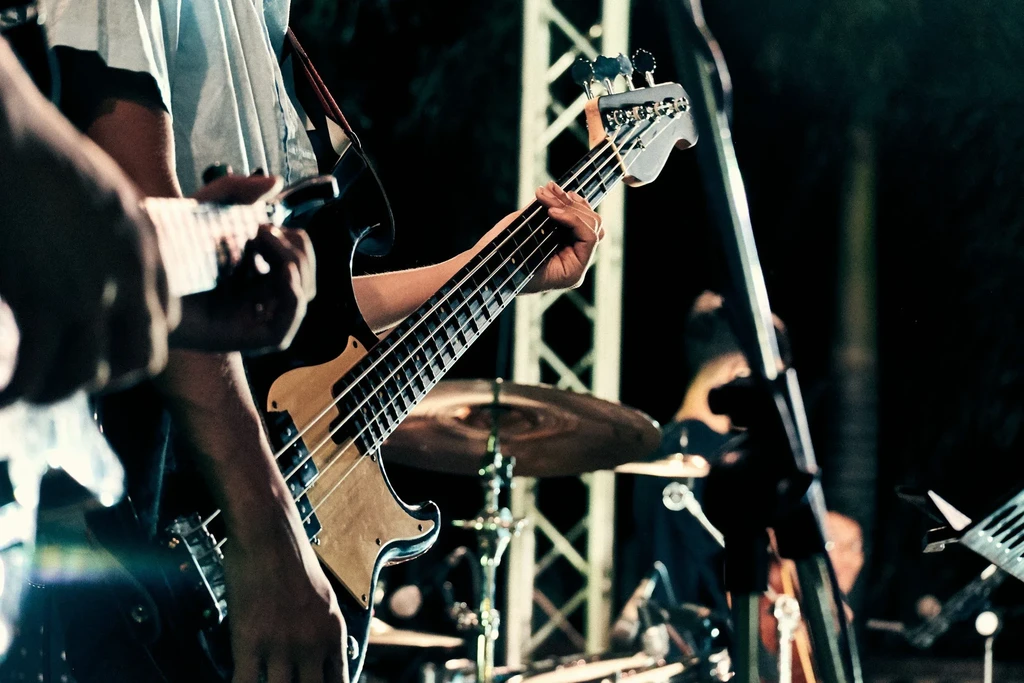Musician's hands playing a black bass guitar on a dark stage.