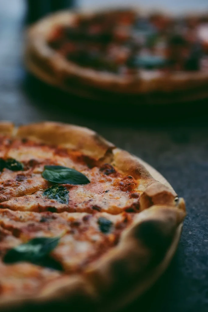 Sliced pizza with melted cheese, tomato, and fresh basil on a dark table.