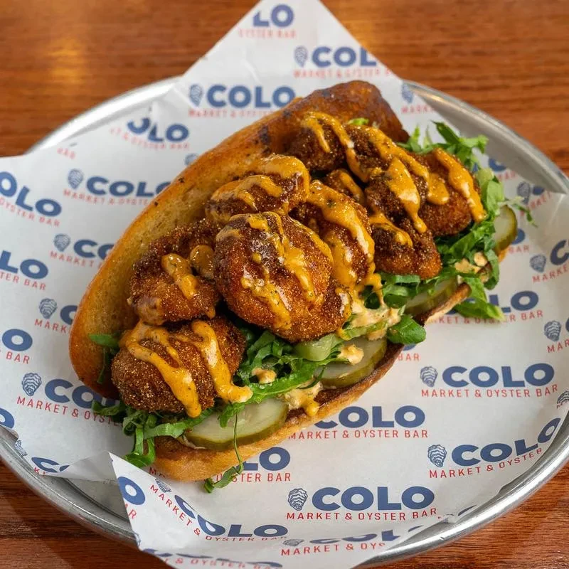Fried seafood sandwich with lettuce, pickles, and sauce on a branded tray.
