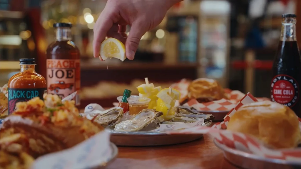 Hand squeezing lemon over fresh oysters on ice, close-up.