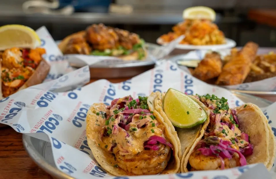 Two seafood tacos with creamy sauce, cabbage, lime, on branded paper.
