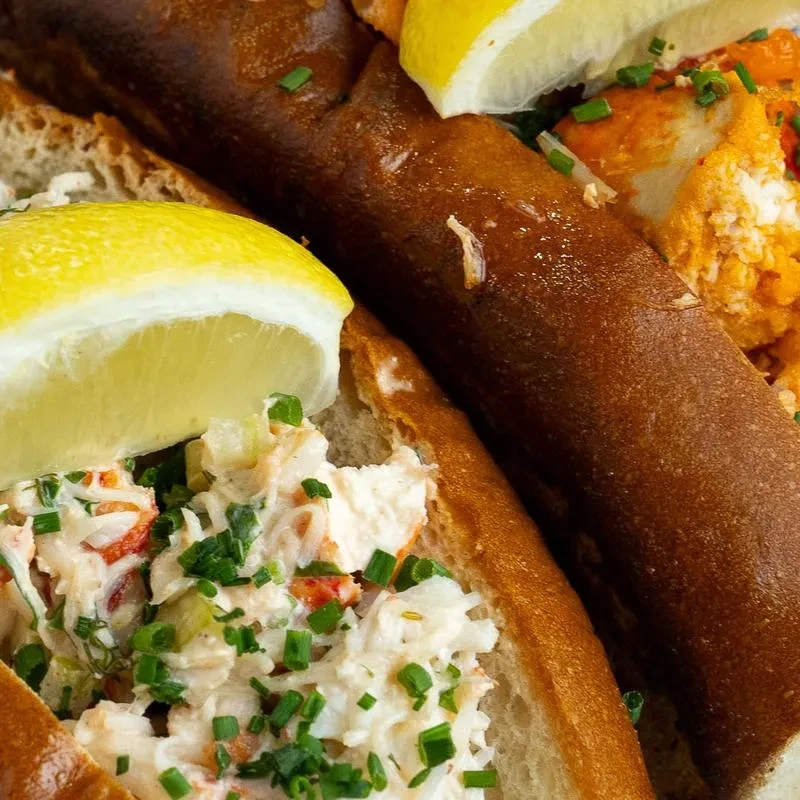 Toasted lobster roll garnished with chives and lemon wedges.