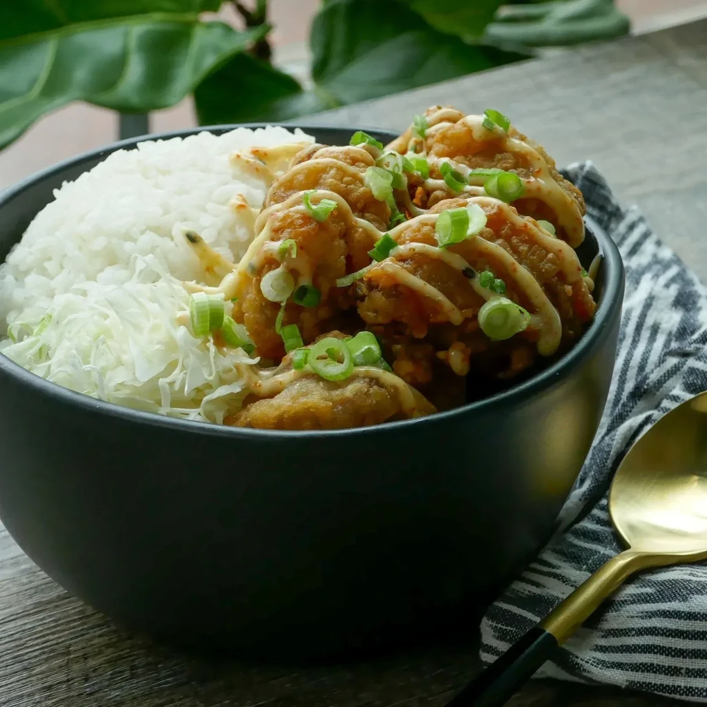 Black bowl of fried chicken, rice, cabbage, sauce, and green onions.