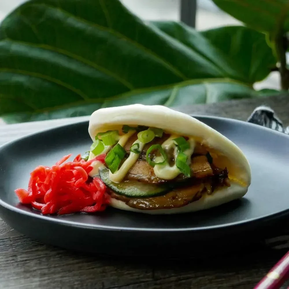 Open bao bun with savory filling, cucumber, green onions, and red ginger.