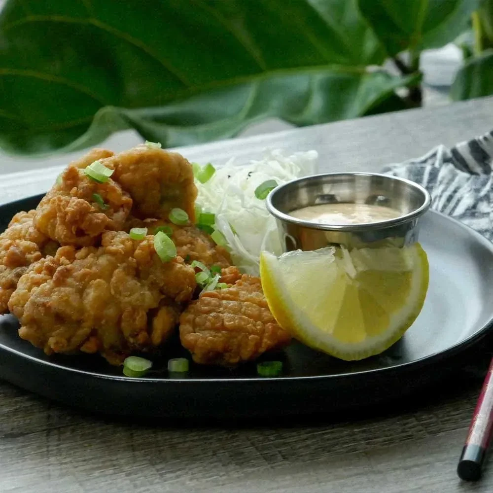 Golden fried pieces, green onions, cabbage, sauce, lemon on black plate.