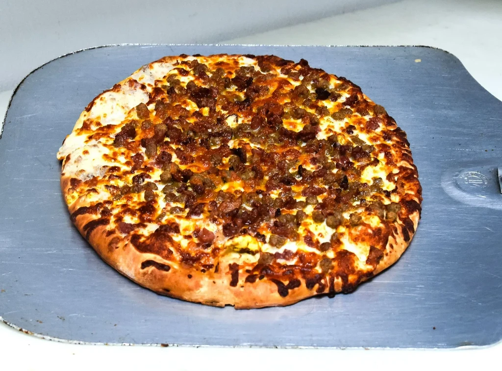 Freshly baked pizza with cheese and crumbled meat on a silver peel.