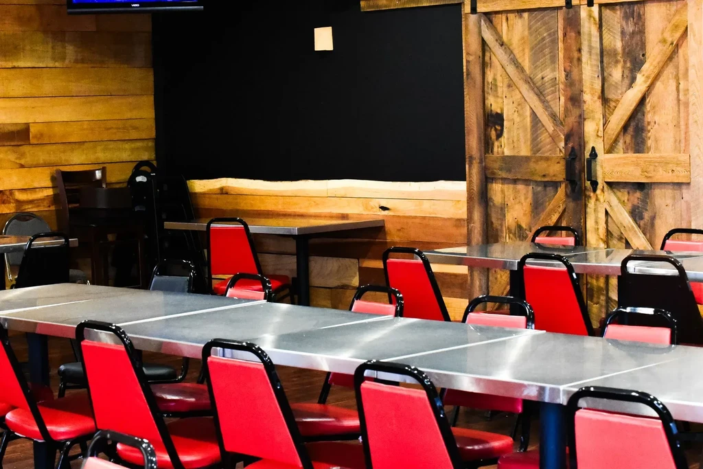 Casual restaurant interior: metallic tables, red chairs, wood paneling, barn door.