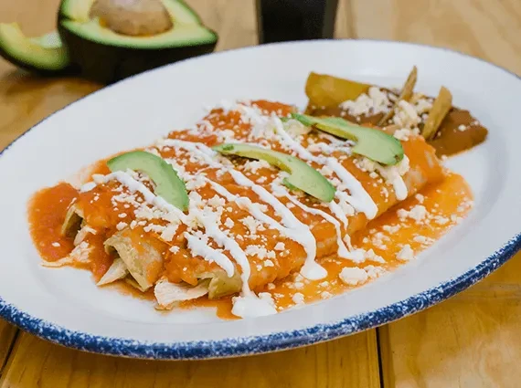 Close-up: Enchiladas with red sauce, cheese, avocado, and fried potatoes.